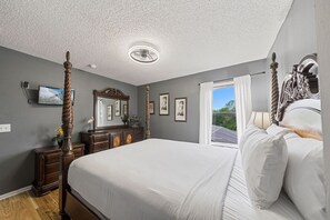 Una camera da letto con un letto a baldacchino, una ventola a soffitto, un'ampia finestra con tende e quadri appesi al muro.