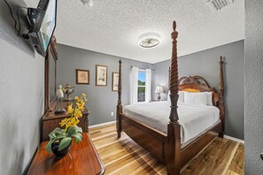 Ein Schlafzimmer mit Himmelbett, Holzboden, Deckenventilator und einem an der Wand befestigten Fernseher.