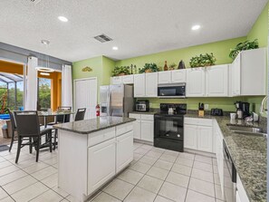 A modern kitchen with white cabinets, granite countertops, and a central island. - Sleeps 16·Pvt Pool·Spa·Game Room·Near Disney (Kissimmee)