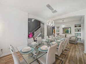 A modern dining area with a glass table, white chairs, and a staircase leading to another level. - Sleeps 16·Pvt Pool·Spa·Game Room·Near Disney (Kissimmee)