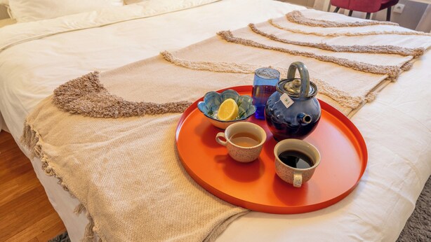 Una cama con una bandeja de desayuno que incluye una tetera, tazas y un vaso de agua.