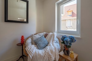 Una habitación acogedora con una cama redonda, una mesita con un florero y un ventanal con vista a un edificio.