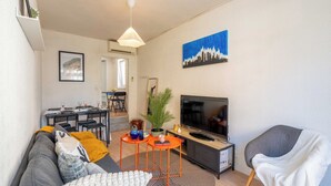 Una sala de estar con sofá, televisor y un comedor con sillas y mesa.