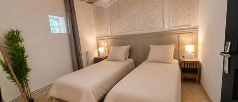 A hotel room with two beds, a large window, a hanging light fixture, and a plant.
