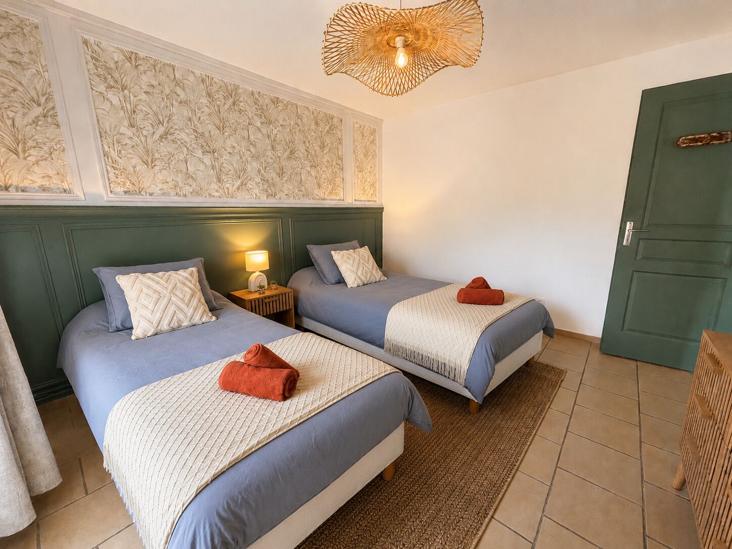 Quarto com duas camas, uma porta verde e parede estampada.