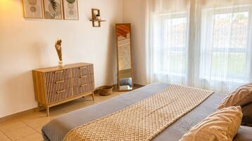 Een slaapkamer met een bed, een houten dressoir, een spiegel en kunst aan de muur.
