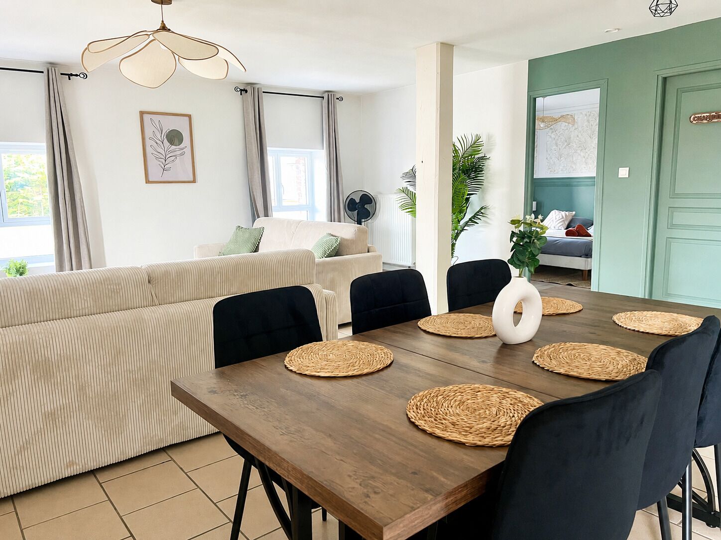 A dining area with a wooden table, black chairs, woven placemats, and a modern pendant light.