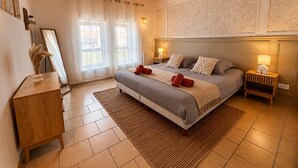 A bedroom with a bed, bedside tables, a mirror, a wooden dresser, and a window with sheer curtains.