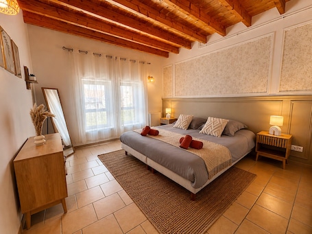A bedroom with a bed, bedside tables, a mirror, a wooden dresser, and a window with sheer curtains.. Apart'Moment - Résidence La Brasserie