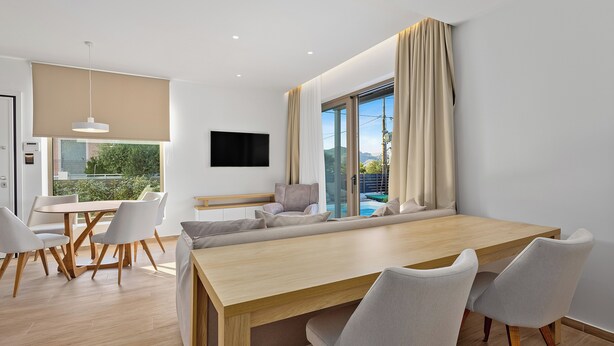 Une pièce moderne avec une table à manger en bois, des chaises blanches, un canapé et un téléviseur fixé au mur.