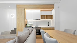 Une cuisine moderne dotée d’appareils électroménagers intégrés, un coin repas avec une table en bois et des chaises à revêtement gris, et un escalier menant à un autre niveau.