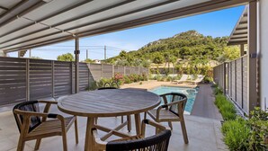 Une terrasse couverte avec une piscine, une table en bois et des chaises.