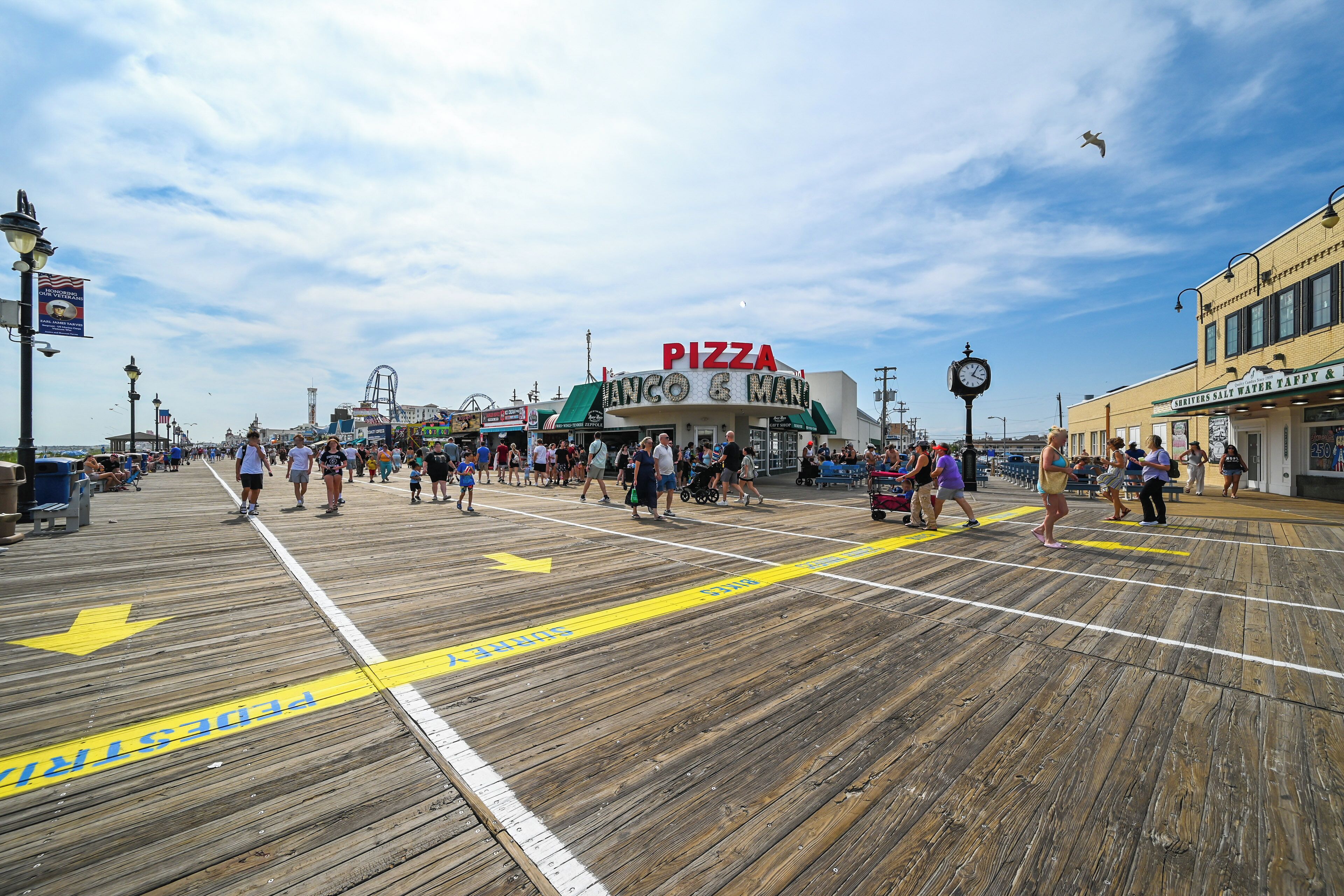 A wooden boardwalk with a pizza restaurant, a Ferris wheel, and a clock tower in the background.