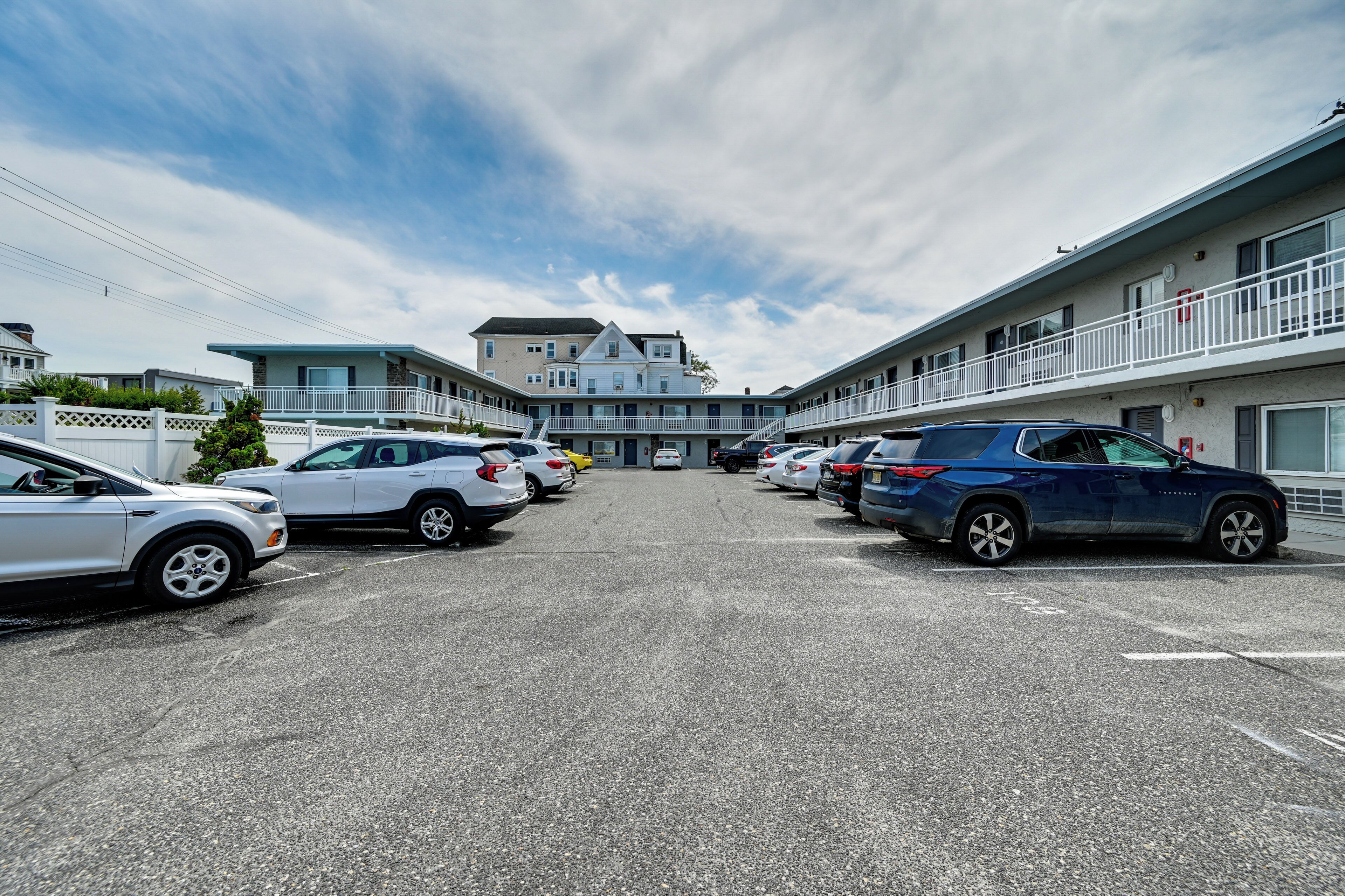 A parking lot with multiple cars, a building with a balcony, and a clear sky.