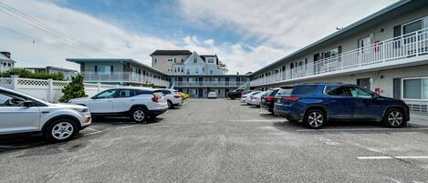 A parking lot with multiple cars, a building with a balcony, and a clear sky.