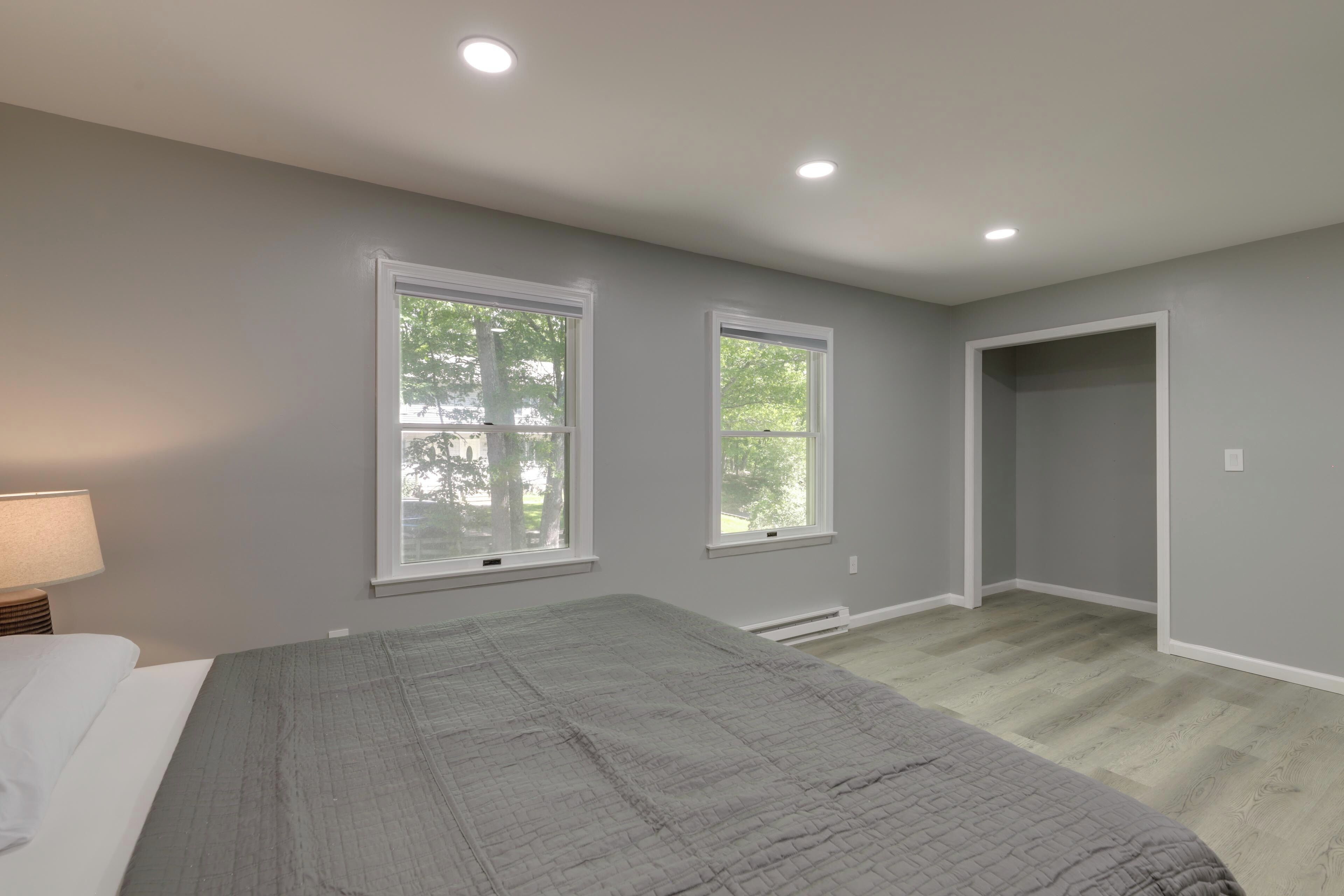 A bedroom with a bed, two windows, a door, and a nightstand with a lamp.