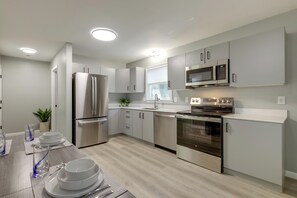 A modern kitchen with stainless steel appliances, light wood flooring, and a clean, minimalist design. - Modern Home, Minutes to Mystic, Casinos and Ocean (Groton)
