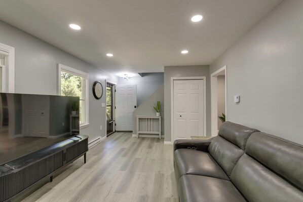 A modern living room with a leather sofa, a flat-screen TV, and a built-in entertainment unit. - Modern Home, Minutes to Mystic, Casinos and Ocean (Groton)