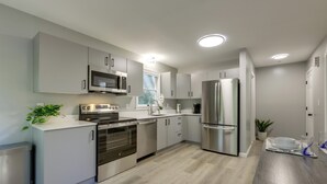 A modern kitchen with stainless steel appliances, white cabinetry, and a wooden floor. - Modern Home Minutes to Mystic, Casinos and Ocean (Groton)