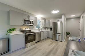 A modern kitchen with stainless steel appliances, white cabinetry, and a wooden floor. - Modern Home Minutes to Mystic, Casinos and Ocean (Groton)