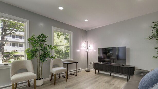A modern living room with a large TV, two chairs, a small table, and a potted plant. - Modern Home Minutes to Mystic, Casinos and Ocean (Groton)