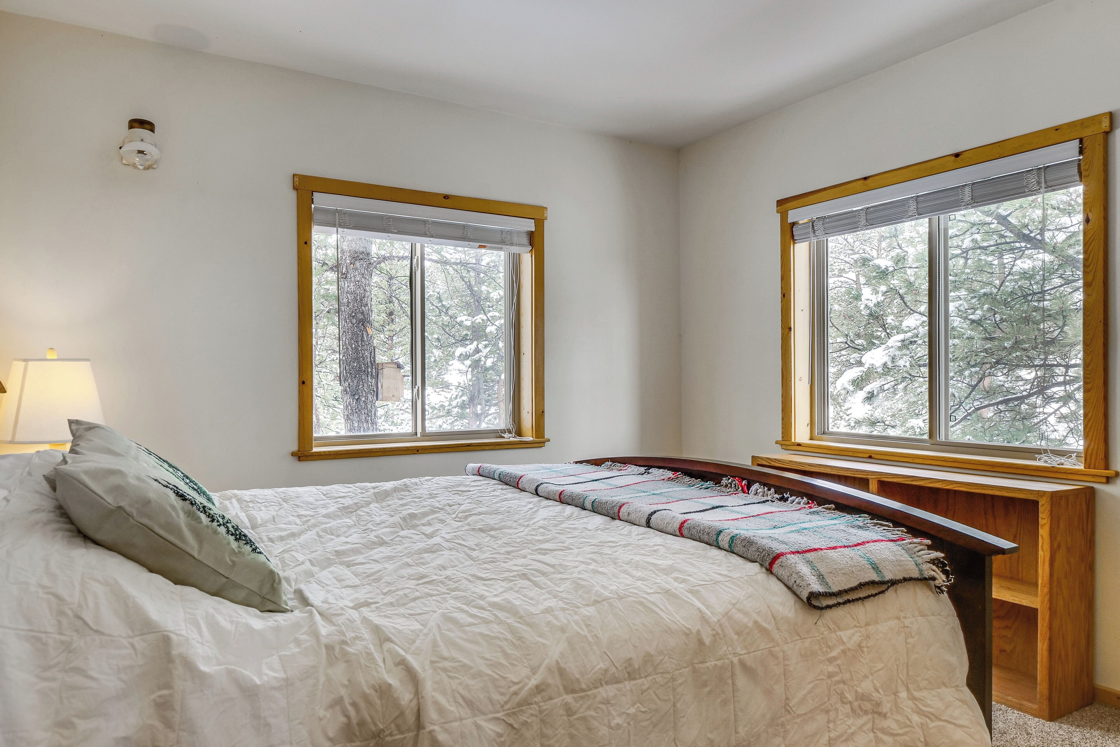 A bedroom with a bed, two windows, a bedside table, and a lamp.