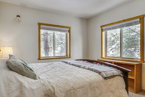 Una camera da letto con un letto, due finestre, un comodino e una lampada.
