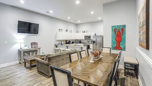 A modern kitchen with white cabinets, a dining area with a wooden table, and a large painting on the wall.