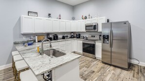 A modern kitchen with white cabinets, a stainless steel refrigerator, a microwave, and a sink.
