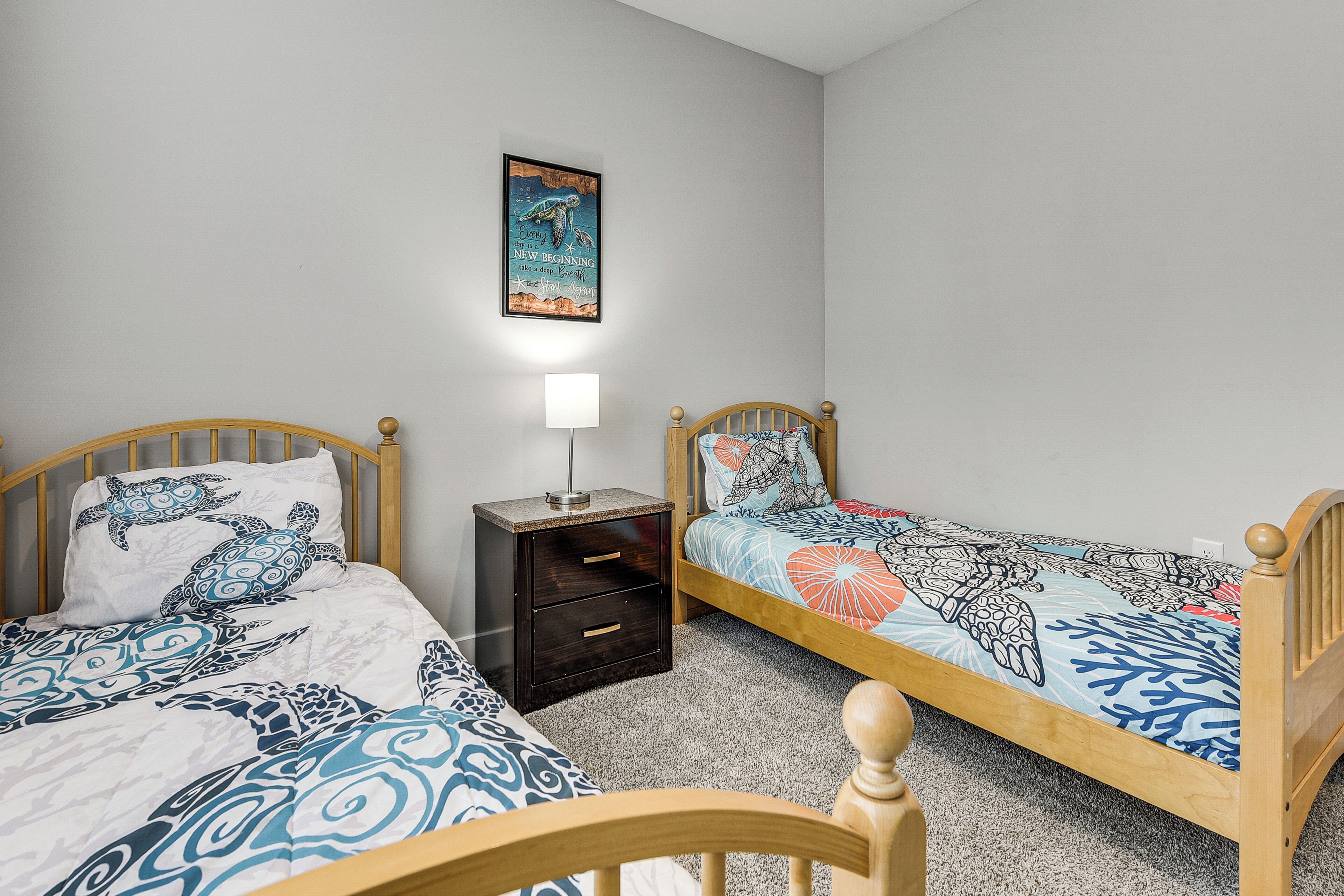 A bedroom with two single beds, a nightstand with a lamp, and a wall-mounted poster.