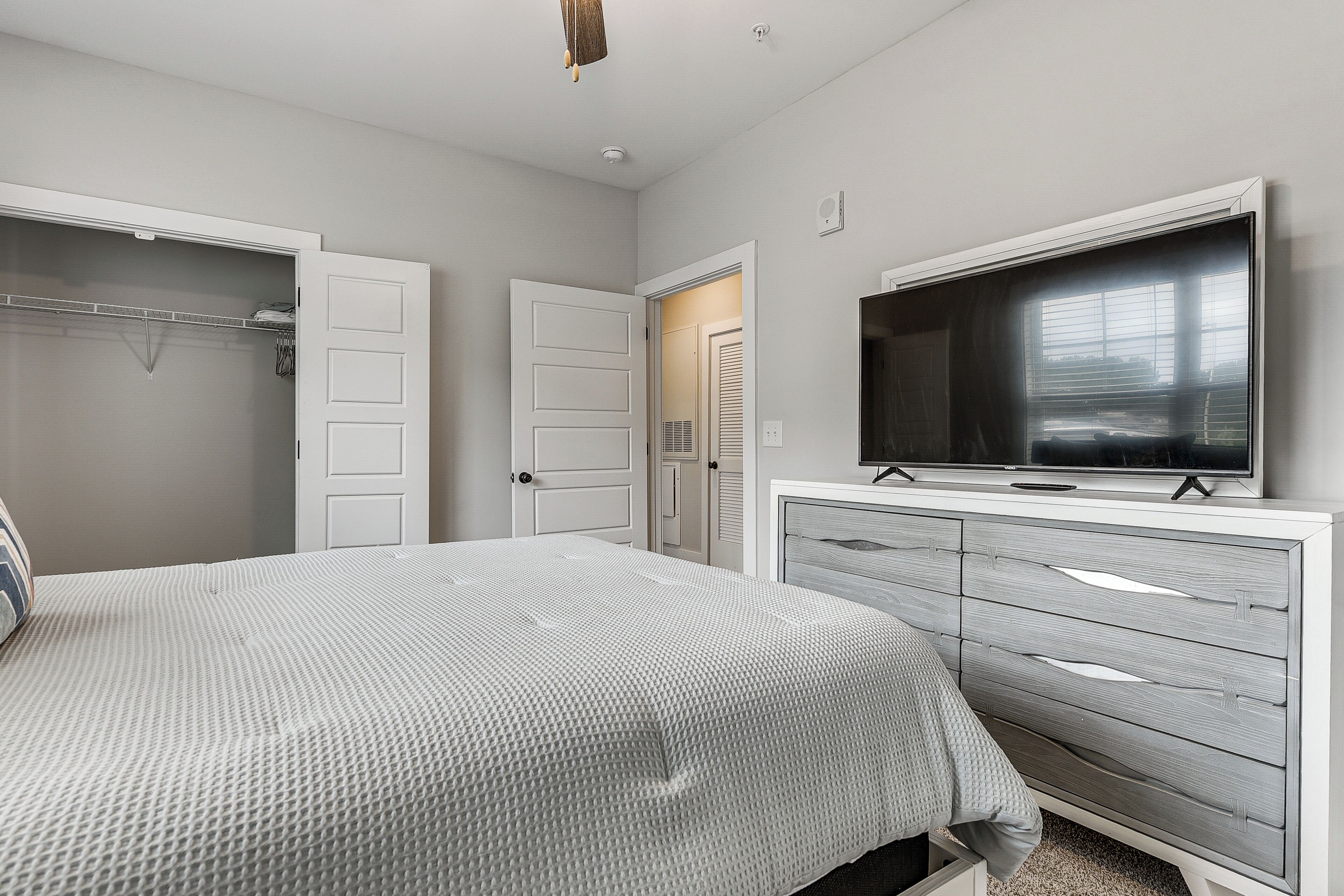 A bedroom with a bed, a dresser, a TV, and two doors.