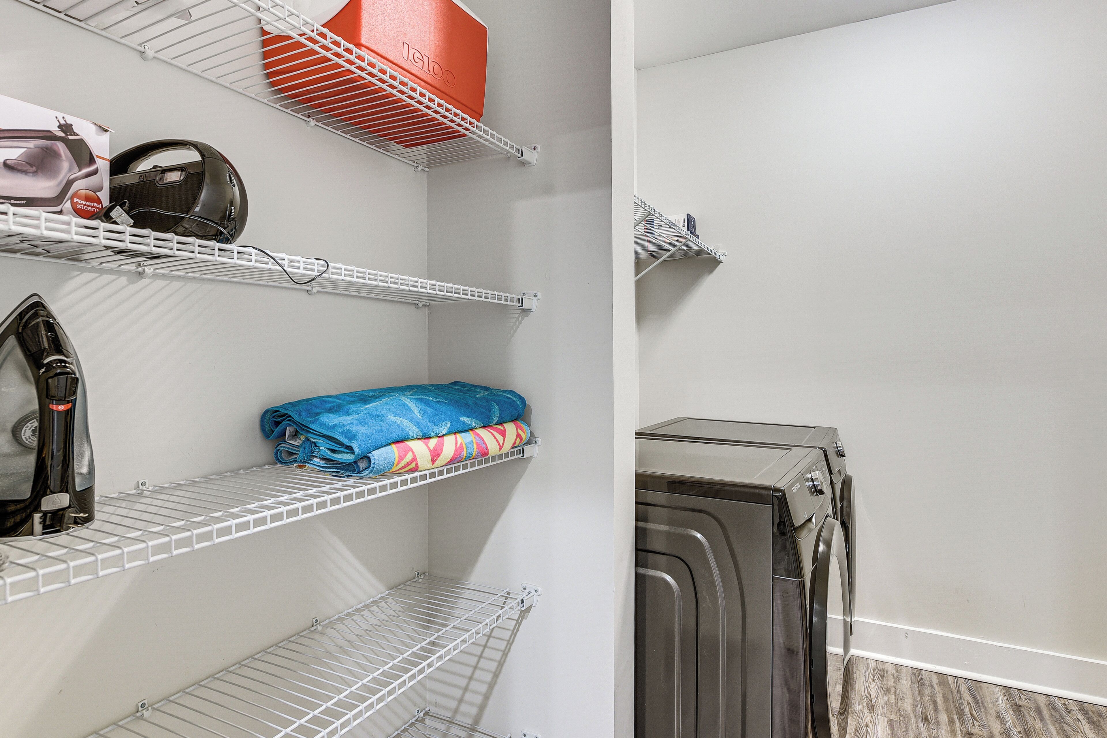 Un espace buanderie comprenant un lave-linge, des étagères avec des vêtements pliés et un aspirateur.