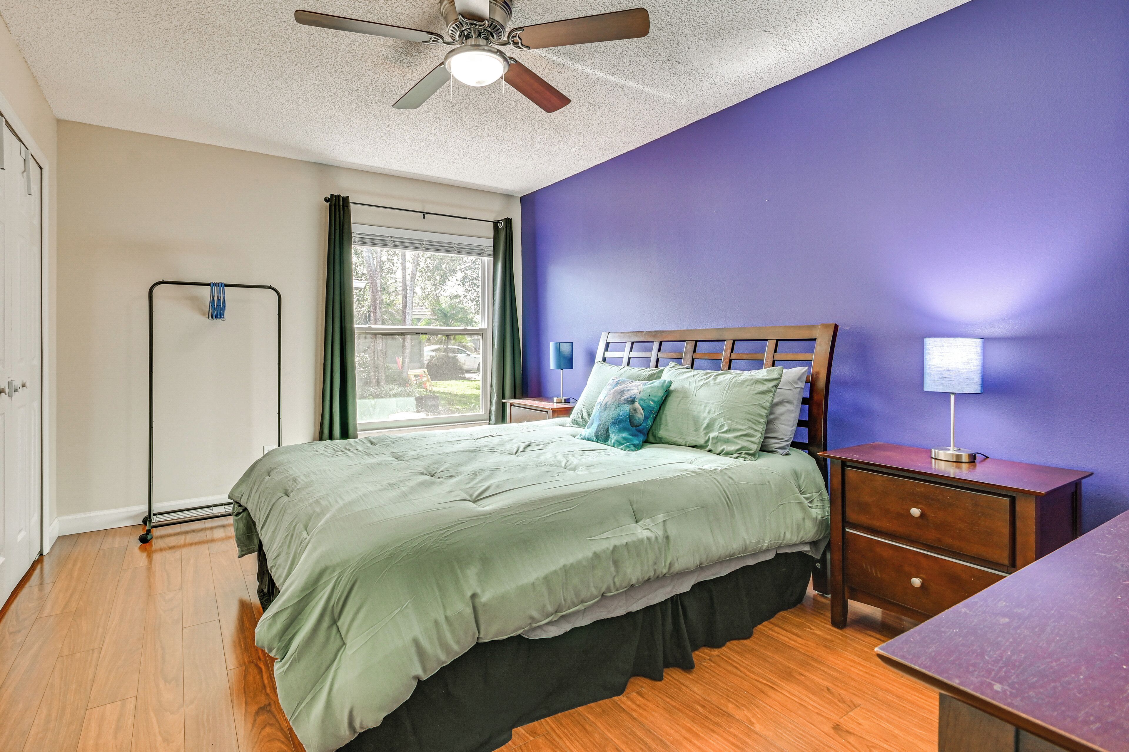 A bedroom with a bed, a nightstand, a dresser, a ceiling fan, and a window with curtains.