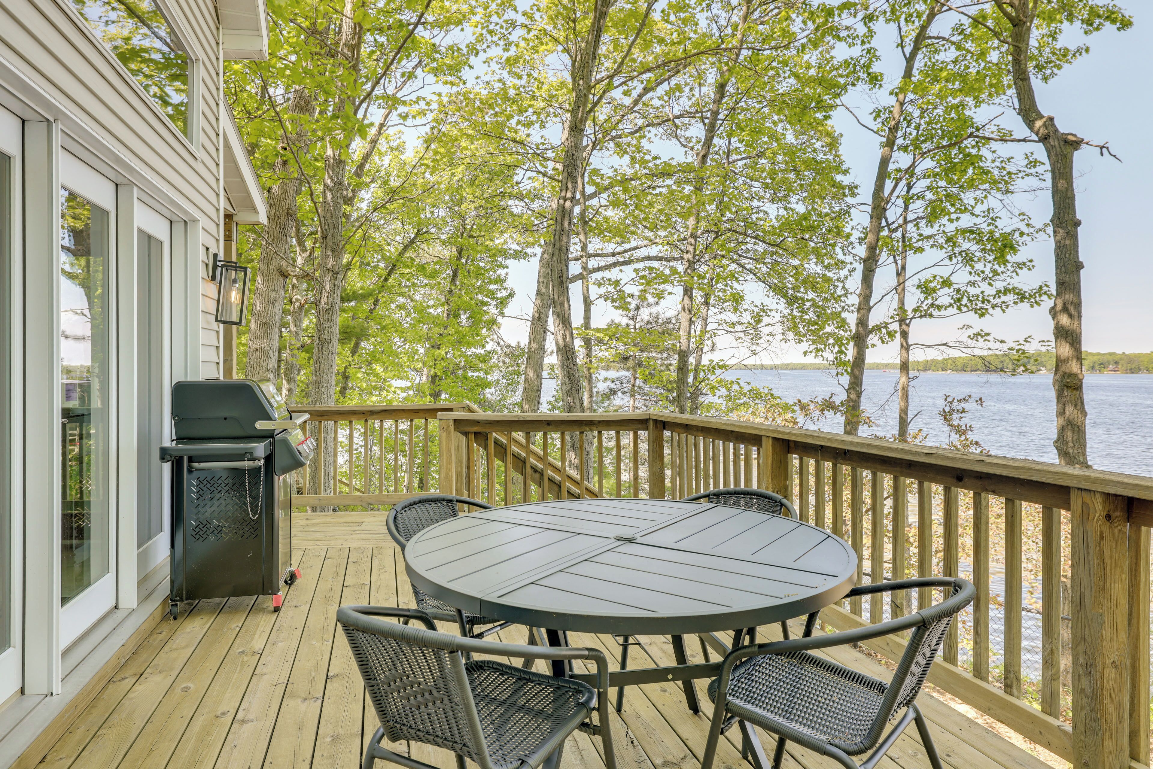A wooden deck with a round table and chairs, a grill, and a view of a lake.