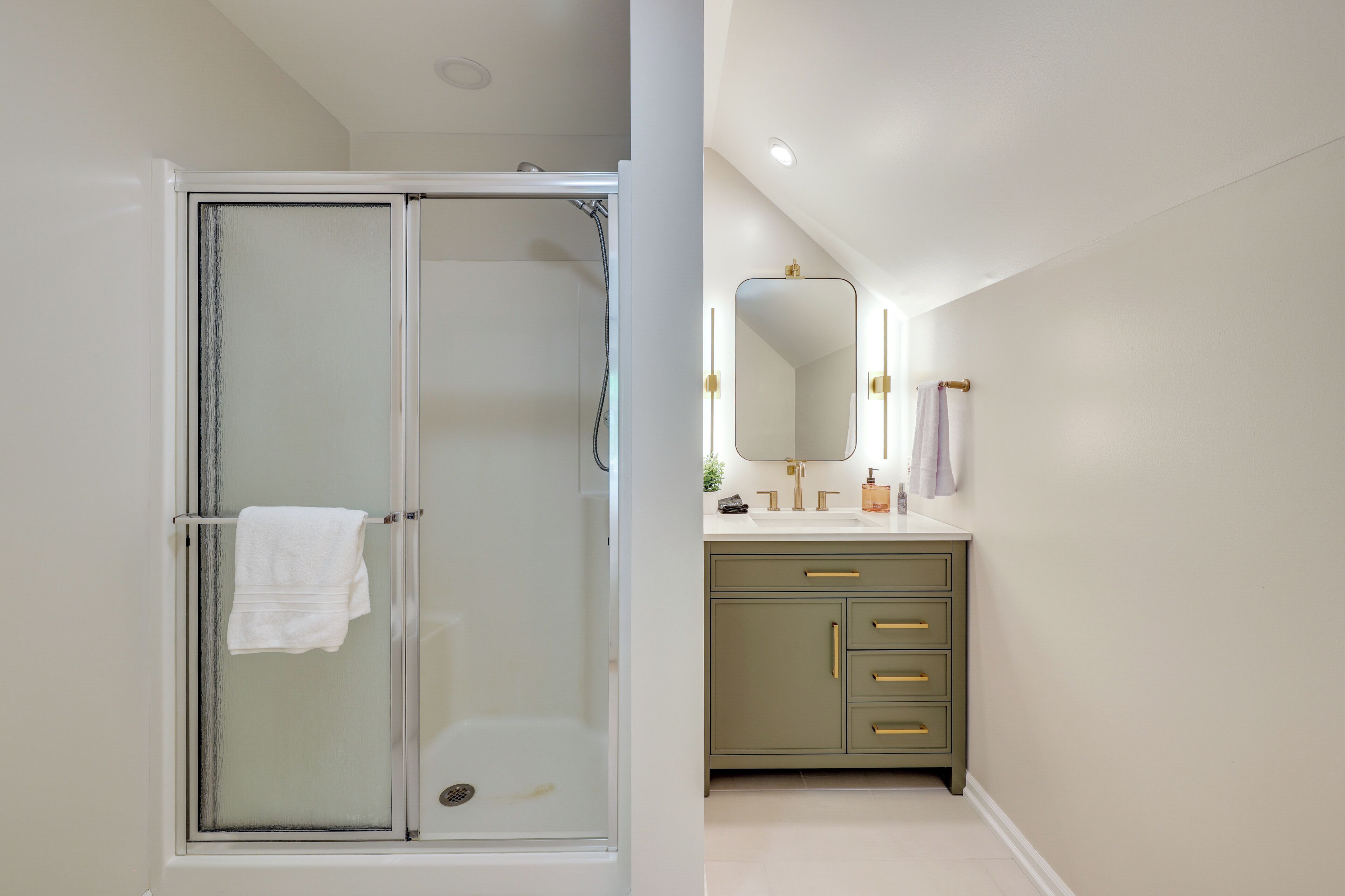 A bathroom with a glass shower enclosure, a vanity with a mirror, and a sink.