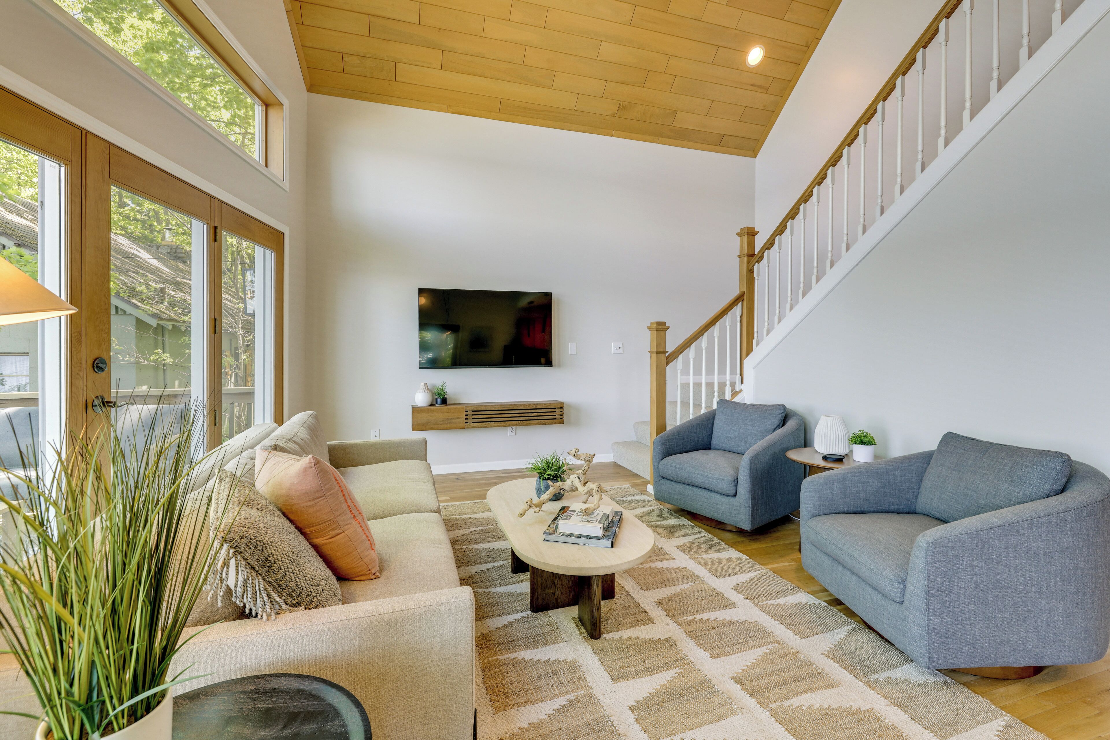 A spacious living room with a high ceiling, a staircase, and a large window.