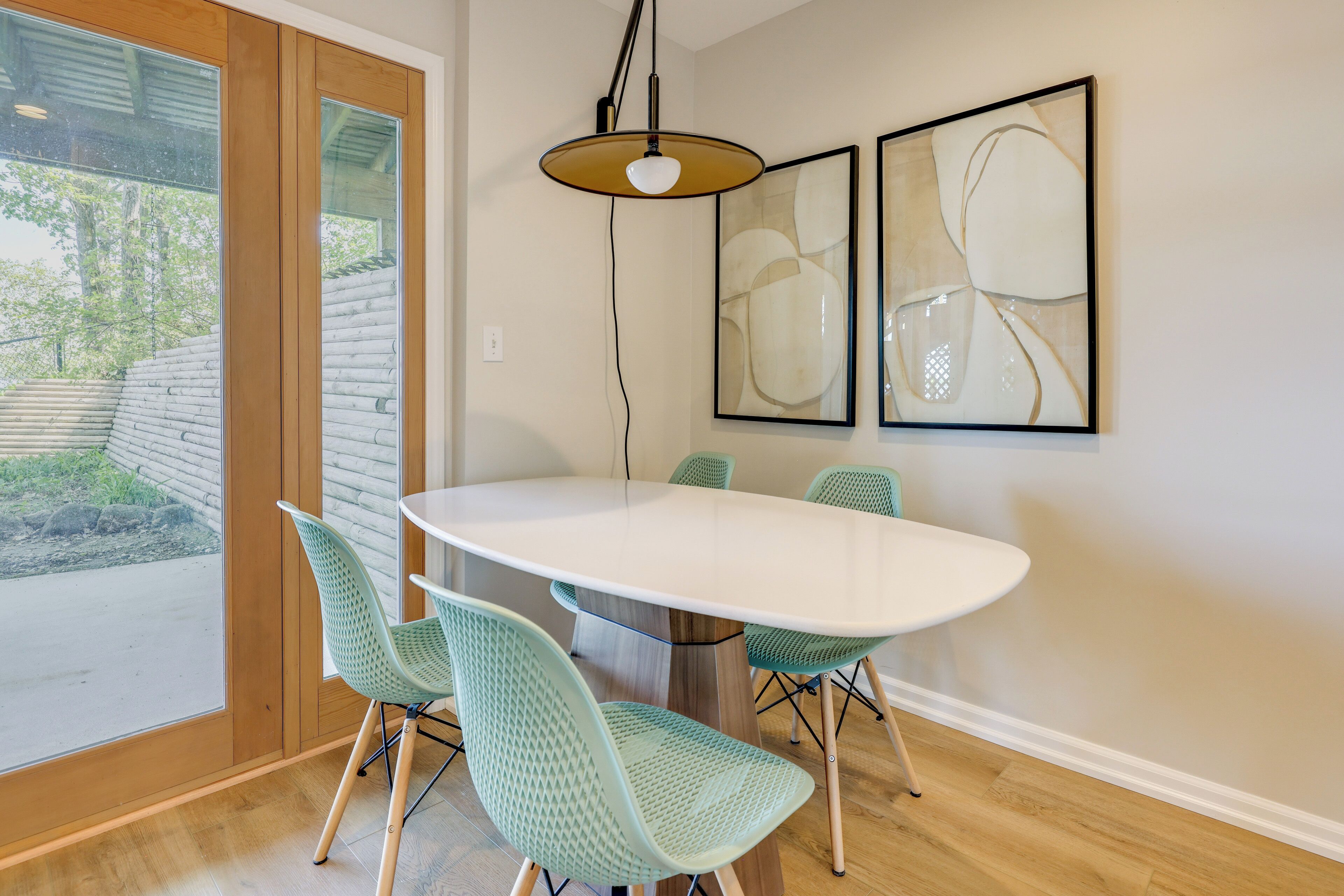 A dining area with a round table, four chairs, a pendant light, and abstract art on the wall.