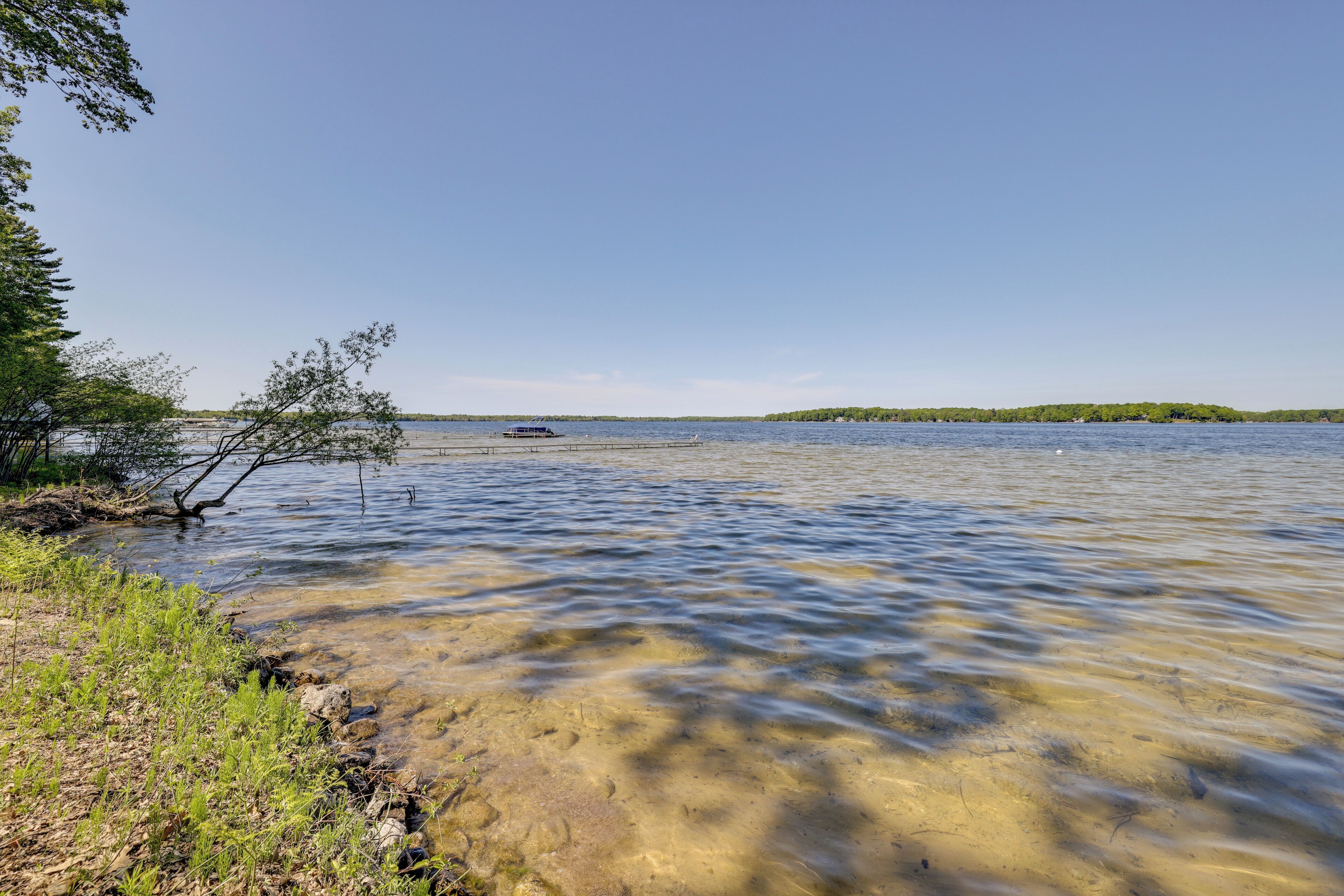 Un lac aux eaux limpides, avec un bateau, une végétation sur les rives et une terre ferme visible au loin.