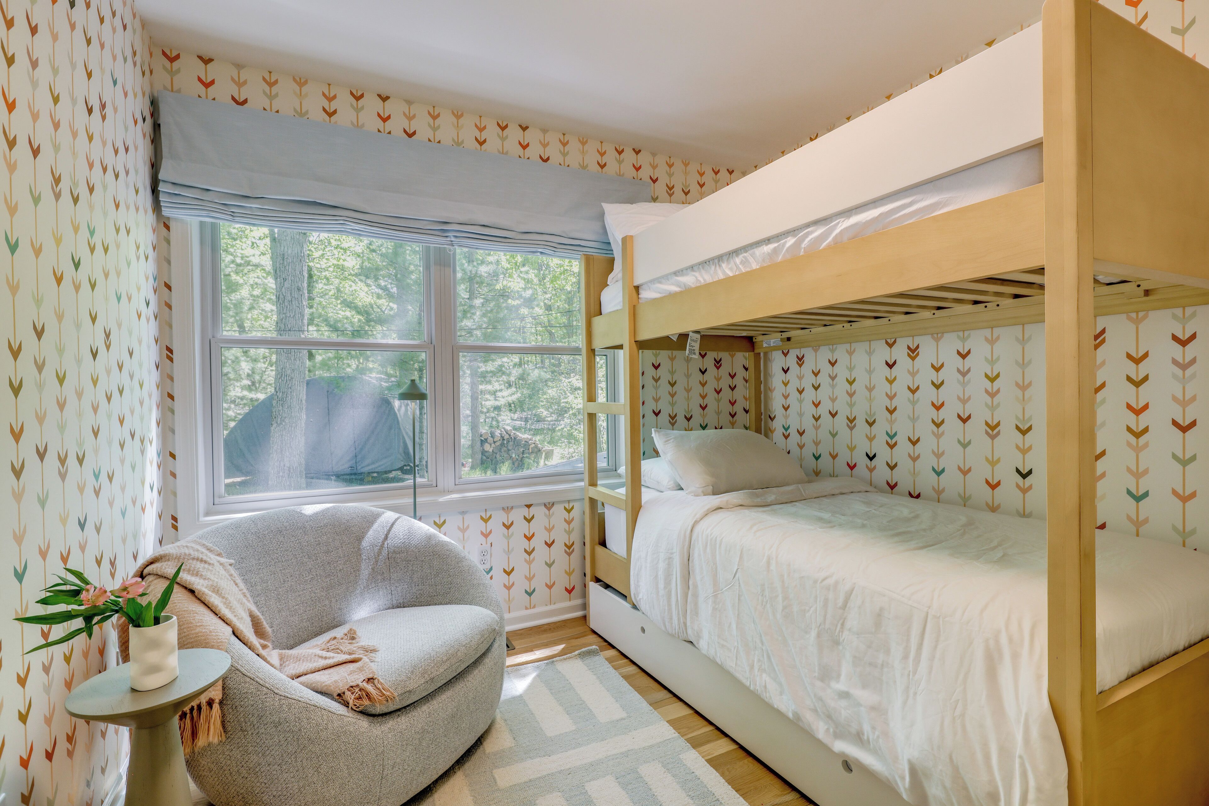 A bunk bed room with a window, a chair, and a small table with a plant.