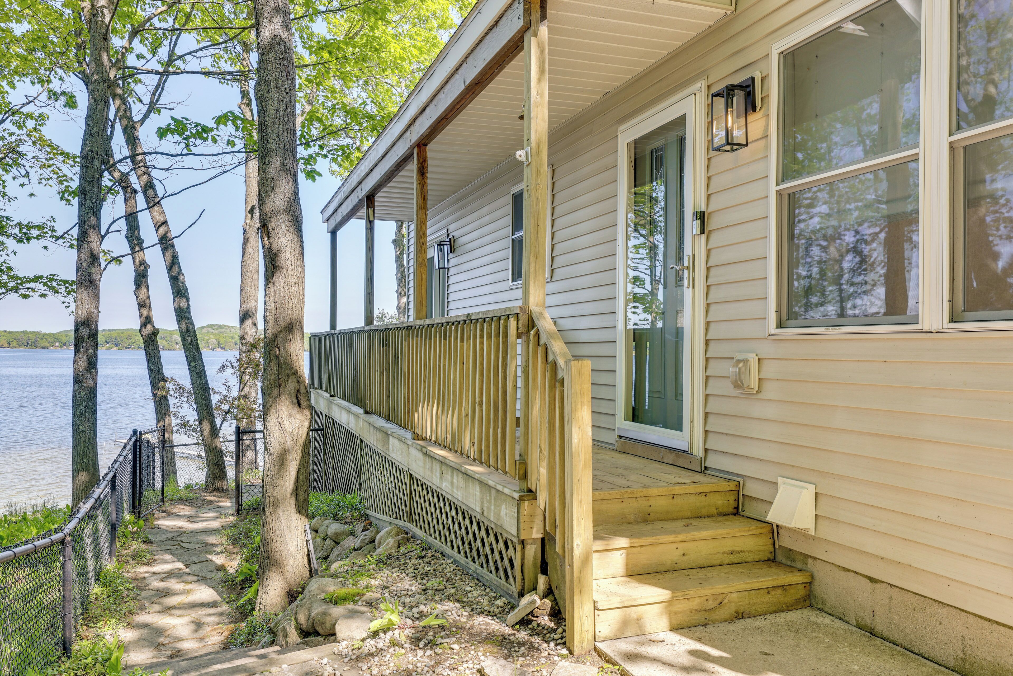 A house with a wooden deck, a front door, and a view of a lake.