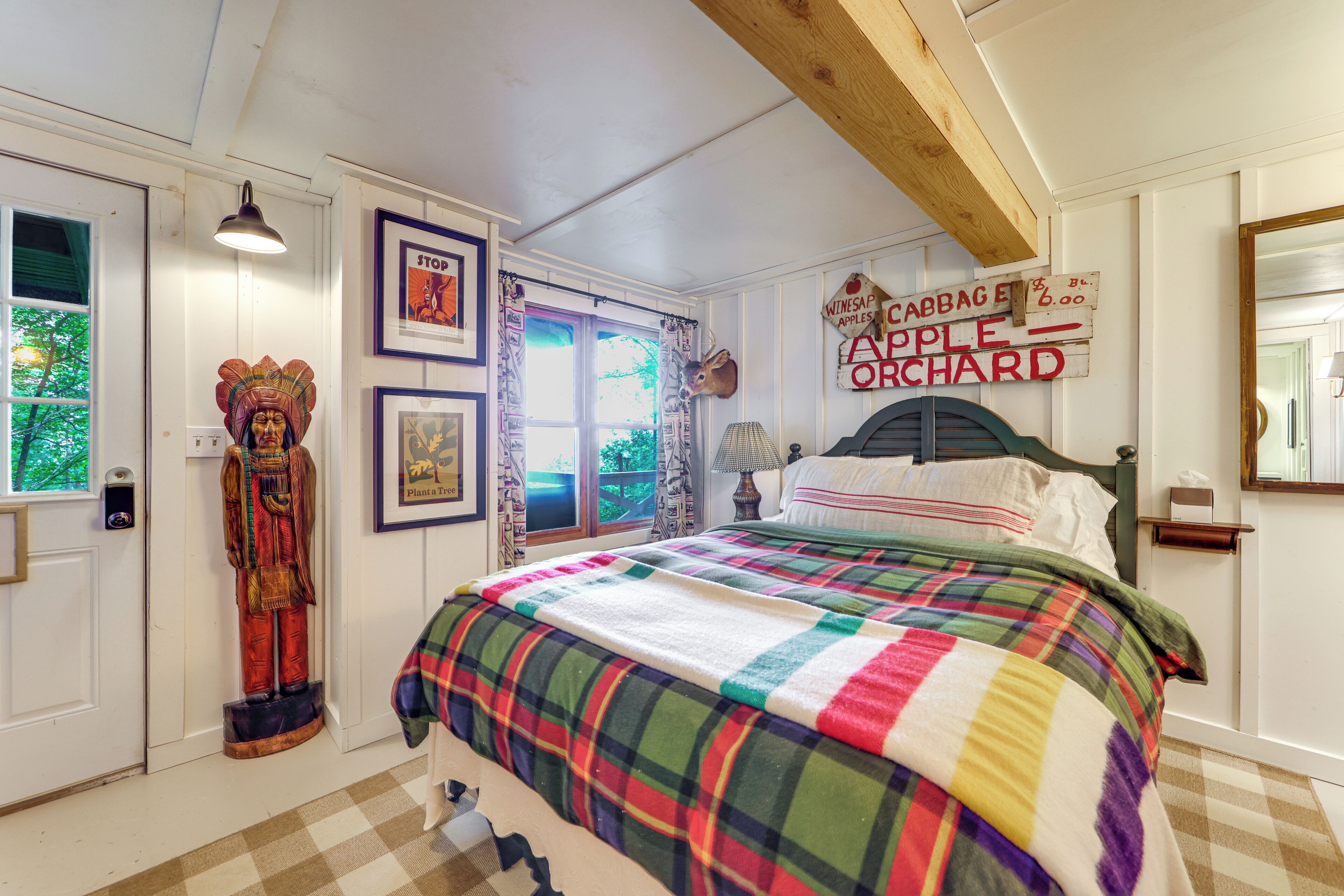 A bedroom with a bed, a window with curtains, a wall-mounted sign, and a door.