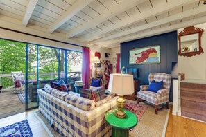 Ein gemütliches Wohnzimmer mit einem karierten Sofa, einem gestreiften Sessel, einem grünen Beistelltisch und einem großen Fenster mit Blick auf Grünflächen.