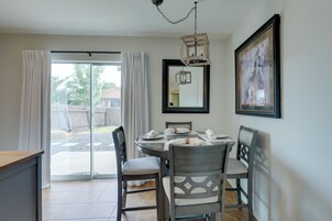 A dining area with a round table, four chairs, a chandelier, a large mirror, and a framed picture on the wall.