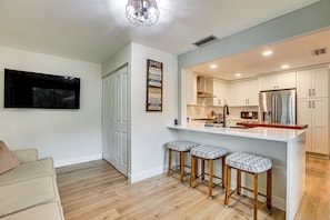 A modern kitchen with white cabinets, a stainless steel refrigerator, and a bar area with stools.