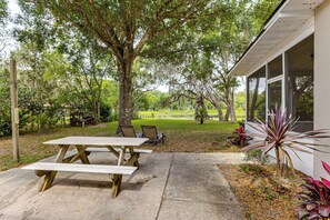 A picnic table with benches, a covered patio area, and a house with a porch.