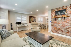 A living room with a sofa, coffee table, TV, and a brick wall with a welcome sign.
