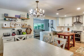 A modern kitchen with a chandelier, white cabinets, and a dining area with a wooden table and chairs.