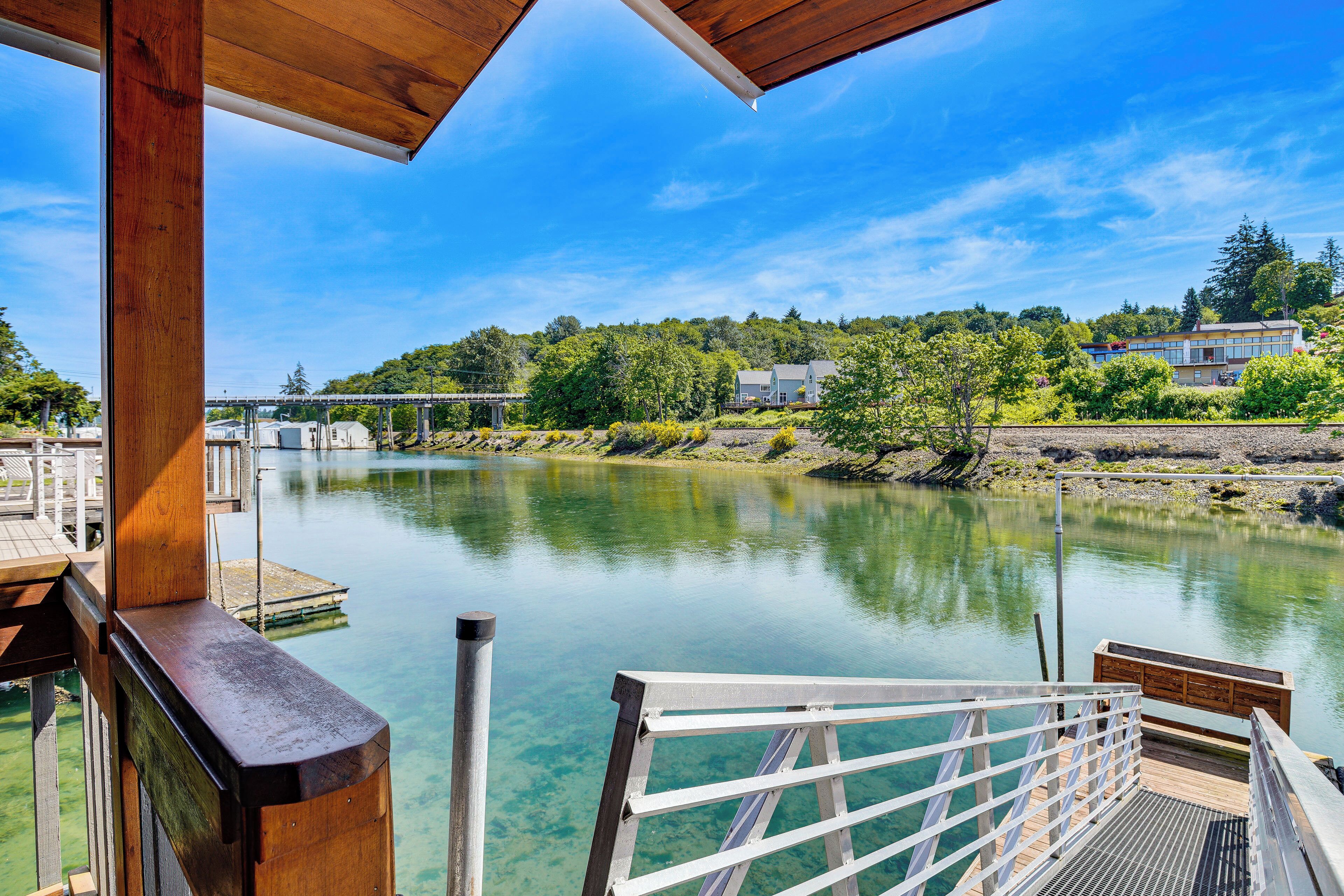 A wooden deck overlooking a calm river with a clear view of houses and trees in the background.