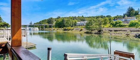 A wooden deck overlooking a calm river with a clear view of houses and trees in the background.