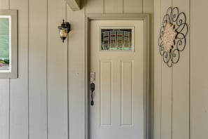 A white door with a keypad lock, a small window with a decorative glass design, and a wall-mounted light fixture. - Pool & Dual Decks! Modern Trinity River Retreat (Douglas City)